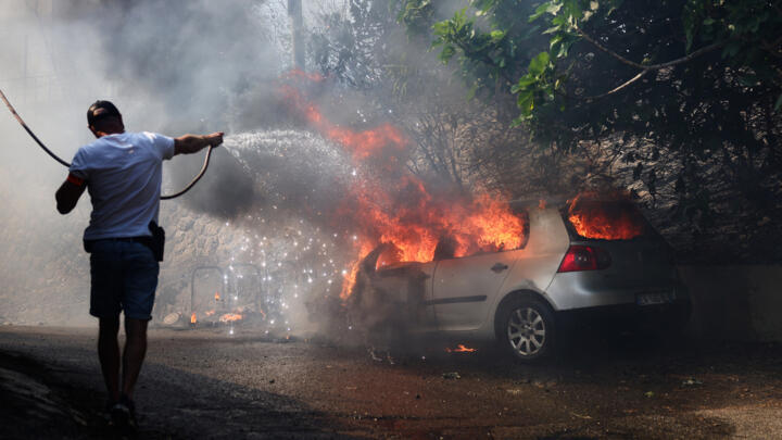 A police officer tries to extinguish a car on fire in L'Estaque, a district of Marseille, on July 8, 2025.