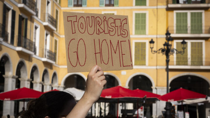A woman holds a sign reading "Tourists go home" during a protest in Palma de Mallorca on June 15, 2025.