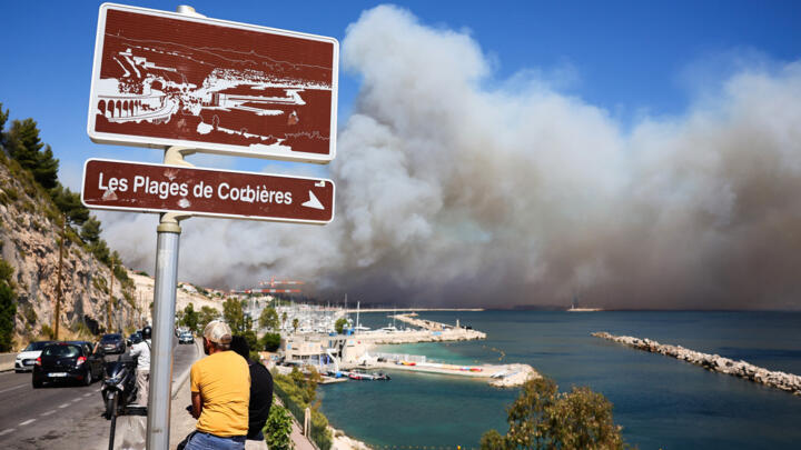 People look on near the Plage des Corbieres, in Marseille, southern France on July 8, 2025, as a smoke from a wildfire rages in the background.