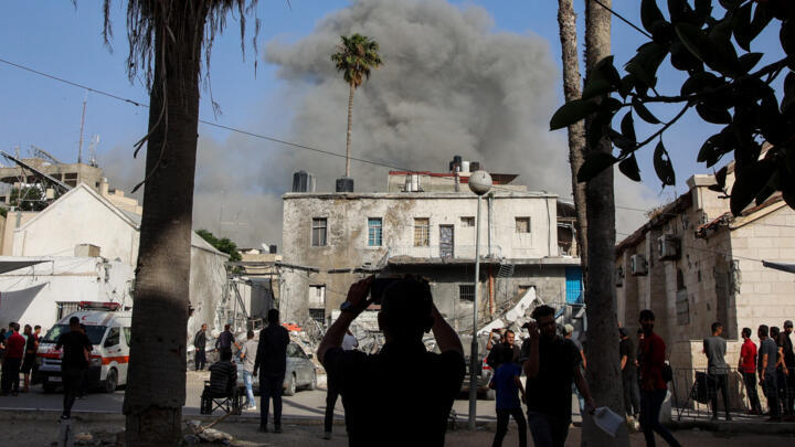 A boy takes a picture of the Ahli Arab Hospital, also known as the Maamadani (Baptist) Hospital, as smoke erupts in the background after an Israeli bombardment of a building in the Daraj neighbourhood, in Gaza City, on May 31, 2025.