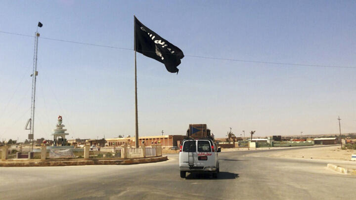 In this July 22, 2014 file photo, a motorist passes by a flag of the Islamic State group in central Rawah, northwest of Baghdad, Iraq.