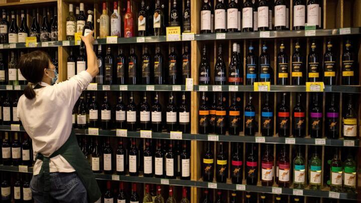 An employee works as Australian-made wine (on display shelves on R) are seen for sale at a store in Beijing on August 18, 2020.