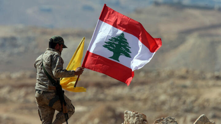 A fighter from the Lebanese Shiite Hezbollah movement holds the Lebanese and the party's flag during a press tour in a mountainous area around the Lebanese border town of Arsal on July 25, 2017.