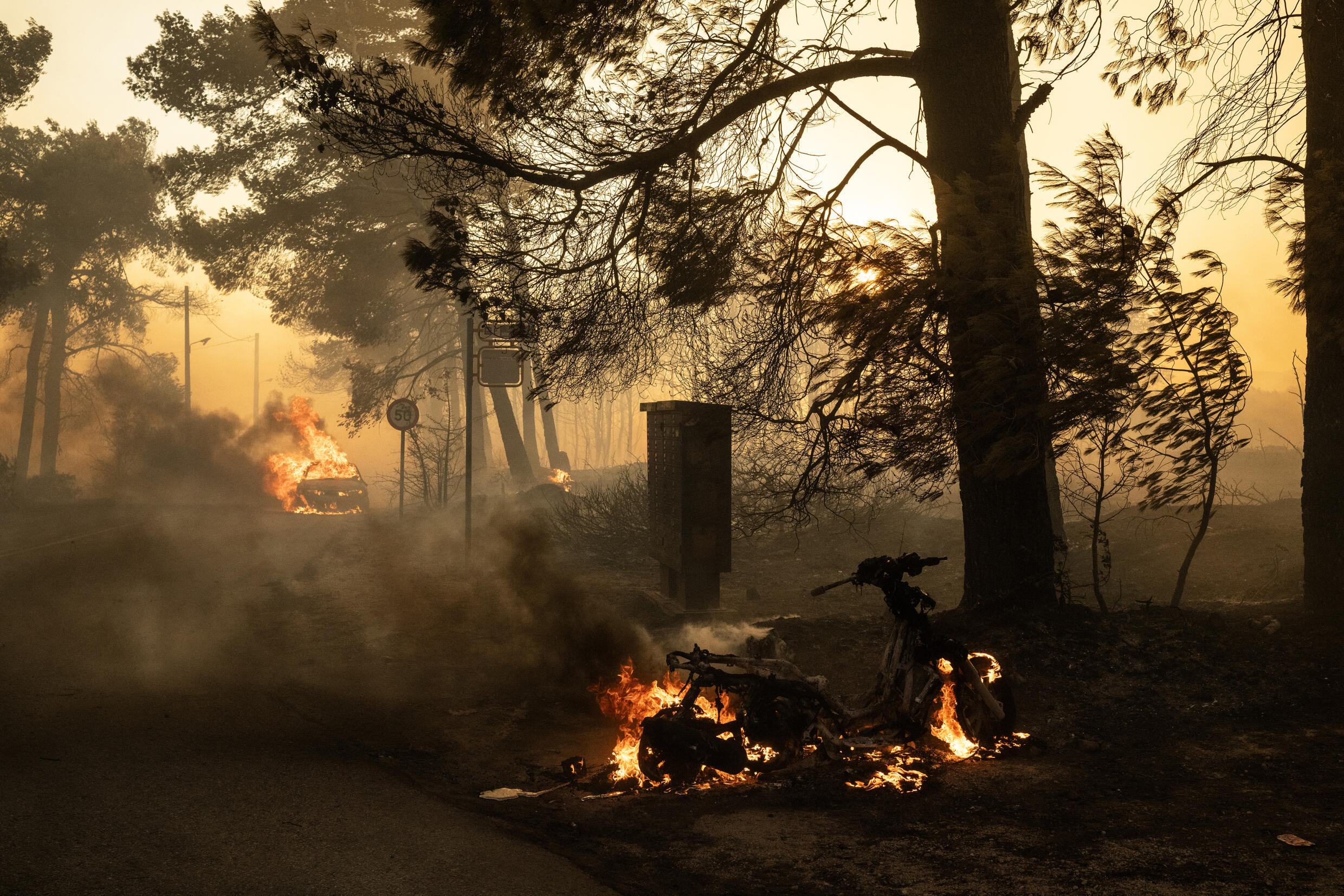 Un scooter et une voiture en flammes lors d'incendies de forêt, le 11 août 2024 à Varnavas, au nord d'Athènes.