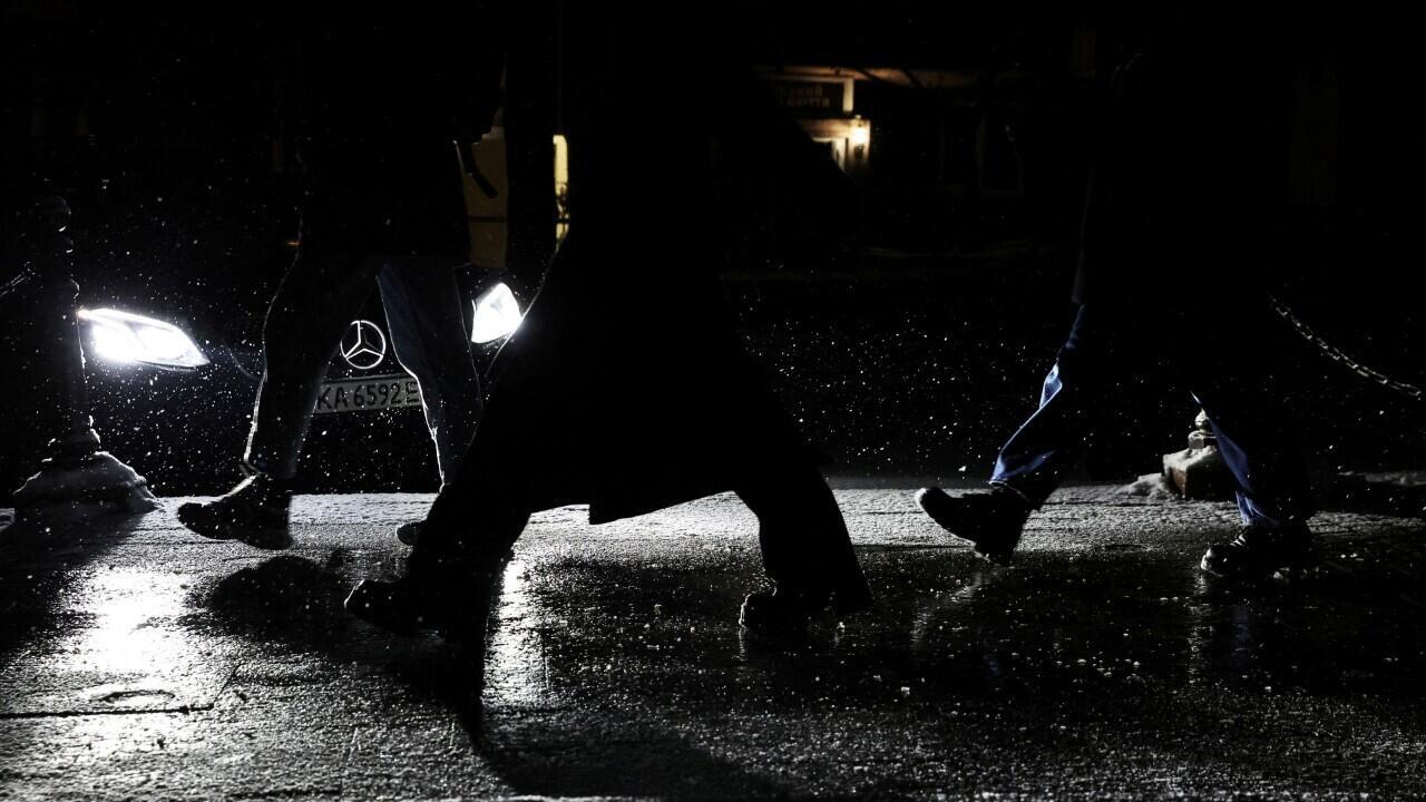 La gente camina por las calles oscurecidas durante los cortes de electricidad mientras cae la nieve en Kyiv, Ucrania, 3 de diciembre de 2022.