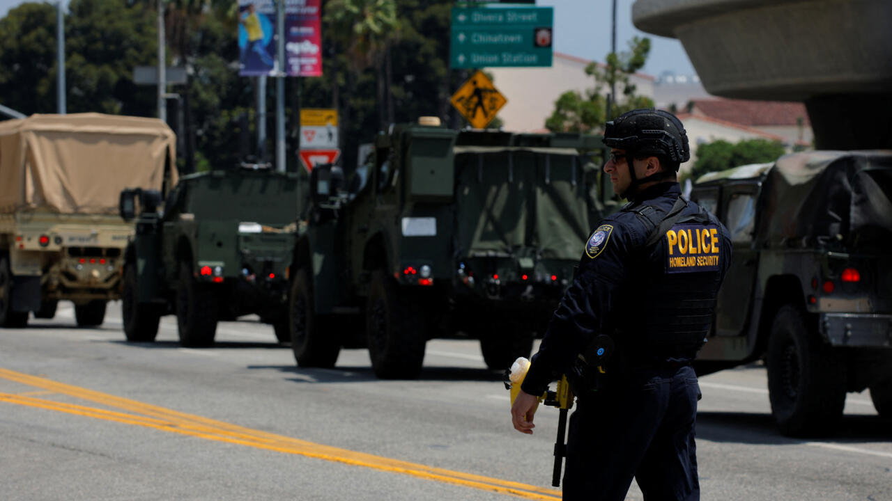 Camiones de la Guardia Nacional circulan mientras un agente de la policía federal observa cerca del edificio federal Edward R. Roybal, tras días de protestas contra las redadas federales de inmigración y el despliegue de la Guardia Nacional de California y la Infantería de Marina de EE. UU., en el centro de Los Ángeles, California, EE. UU., el 10 de junio de 2025.