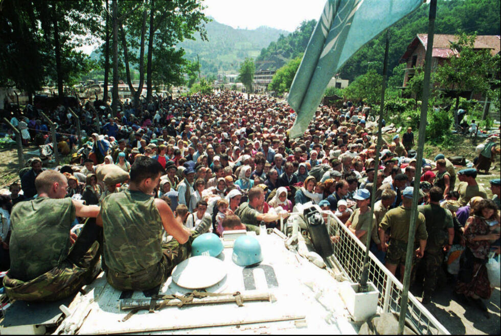 Sur cette photo d'archives du 13 juillet 1995, des Casques bleus néerlandais de l'ONU sont assis sur un véhicule blindé de transport de troupes tandis que des réfugiés musulmans de Srebrenica se rassemblent dans le village voisin de Potocari.