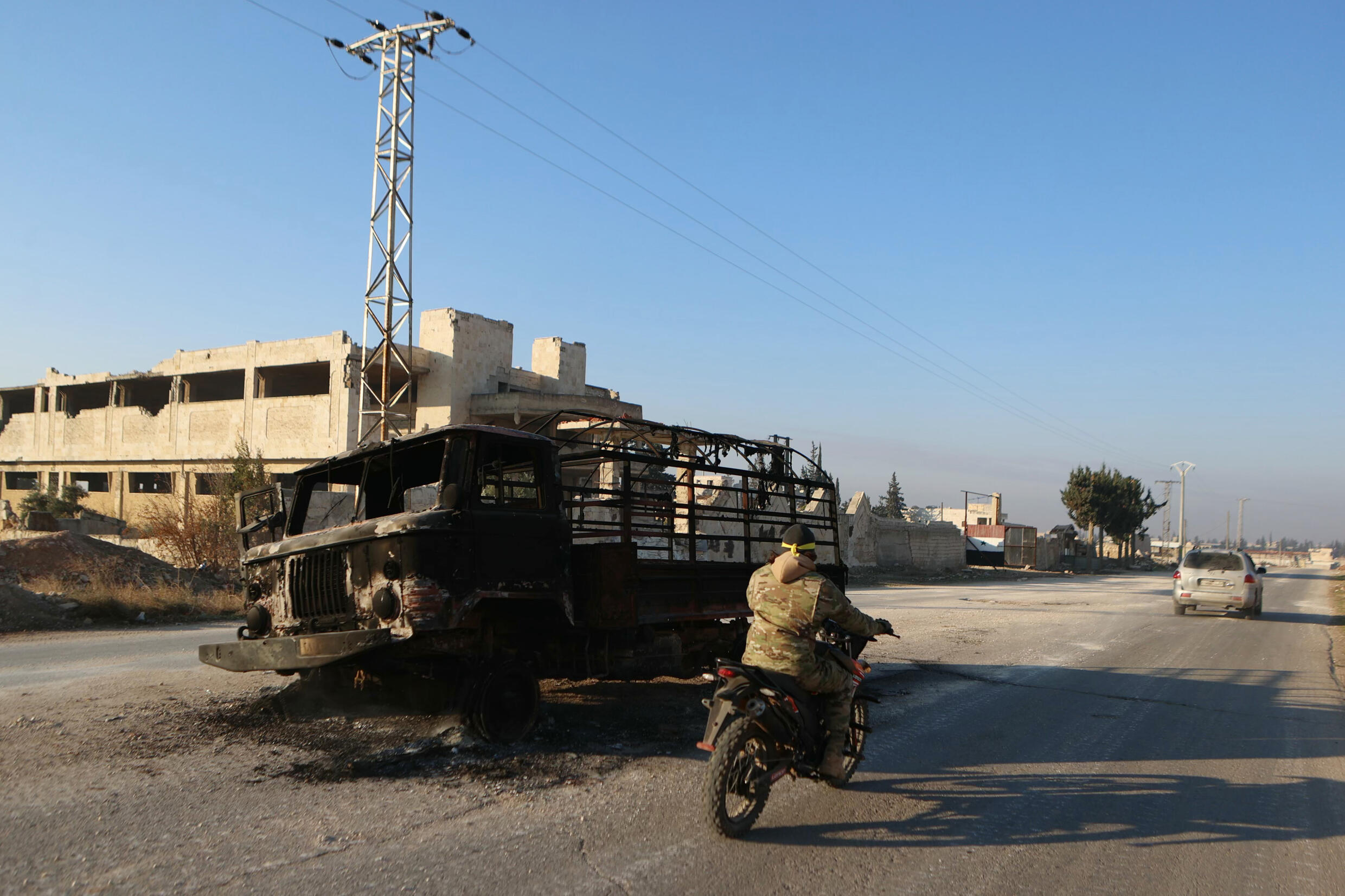 Un combattant près d'un camion calciné à Khan al-Assal, une localité prise par les jihadistes et leurs alliés dans le nord-ouest de la Syrie, le 29 novembre 2024