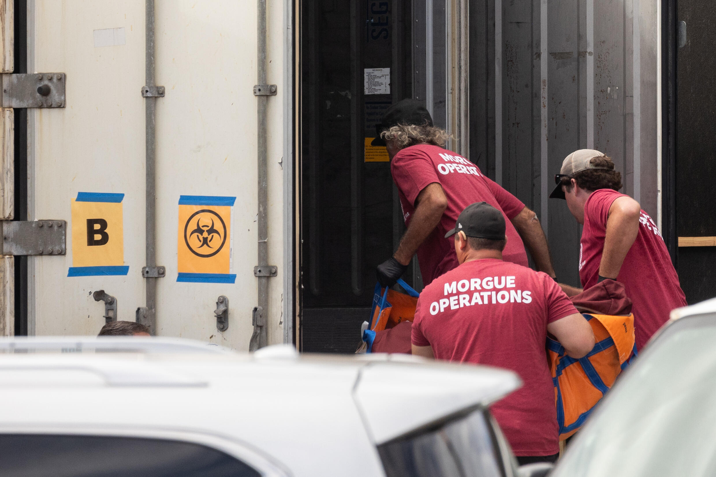 Morgue workers move a body bag into a refrigerated storage container adjacent to the Maui police department's forensic facility, where human remains have been stored in the aftermath of the wildfires.