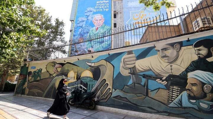 An Iranian woman walks on a sidewalk next to a recently unveiled billboard depicting Israel's Prime Minister Benjamin Netanyahu with text in Persian reading "Hitanyahu".
