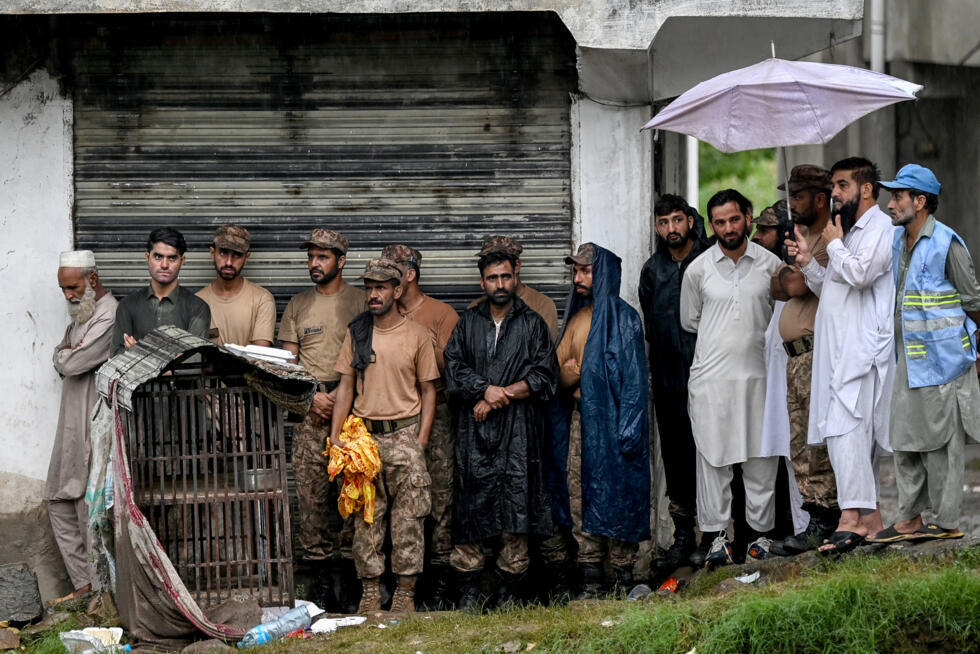 Des sauveteurs et du personnel militaire s'abritent de la pluie sous le toit d'un bâtiment alors que le niveau des eaux de crue monte dans le district de Buner, dans la province de Khyber Pakhtunkhwa, le 18 août 2025 au Pakistan