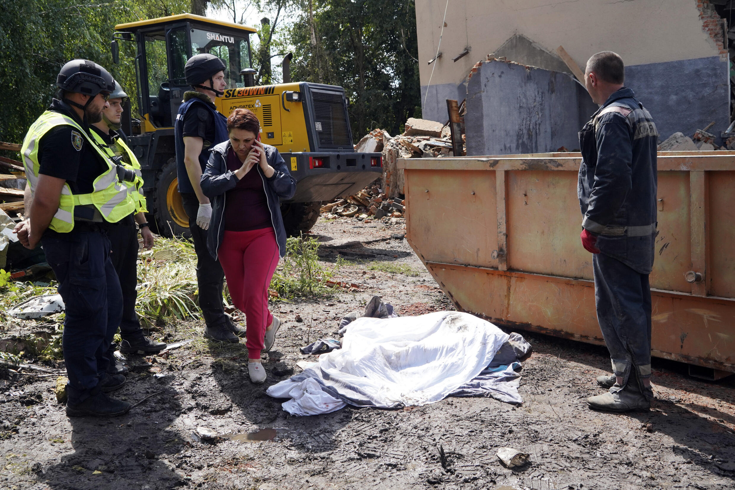 Oficiales de policía, a la izquierda, junto al cuerpo cubierto de una mujer muerta por un ataque con misiles rusos el lunes en Chuhuiv, región de Kharkiv, Ucrania, el martes 26 de julio de 2022.