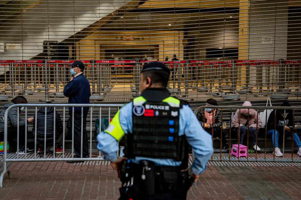 A police officer keeps watch as people wait in line to enter the West Kowloon Law Courts building.
