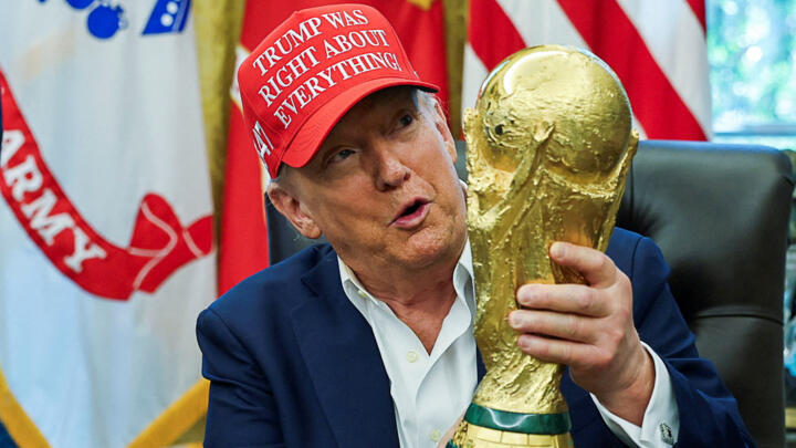 US President Donald Trump wears a 'Trump Was Right About Everything!' hat while holding the FIFA World Cup Trophy in the Oval Office.