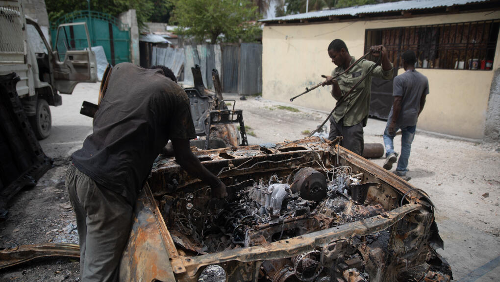 Foto archivo. Hombres rescatan piezas de un auto carbonizado que fue incendiado durante enfrentamientos entre pandillas armadas en el barrio Butte Boyer de Puerto Príncipe, Haití, viernes 13 de mayo de 2022.