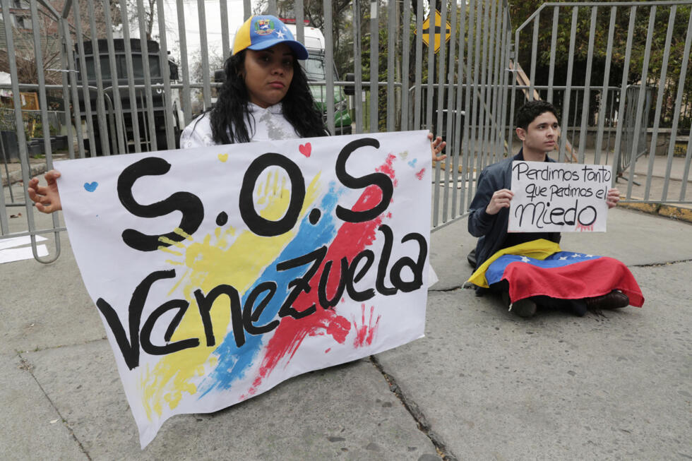Una pareja de ciudadanos venezolanos sostiene carteles afuera de la embajada de Venezuela el 30 de julio de 2024 en el barrio de Providencia en Santiago (Chile).