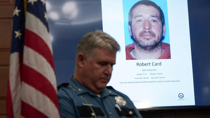 A police officer stands next to a screen displaying a picture of the suspected shooter during a press conference following the deadly mass shooting, at City Hall in Lewiston, Maine, US October 27, 2023.