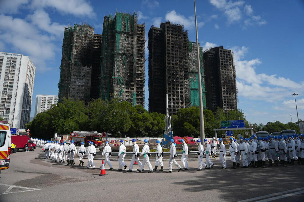 Police officers from the Disaster Victim Identification Unit (DVIU), dressed in white-coloured full-body protective gear, walk past the housing blocks of Wang Fuk Court in the aftermath of the deadly