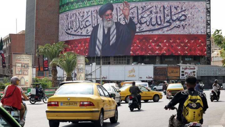 Motorists drive their vehicles past a billboard depicting Iran's Supreme Leader Ayatollah Ali Khamenei displayed in the centre of Tehran's Valiasr Square on July 13, 2025. 