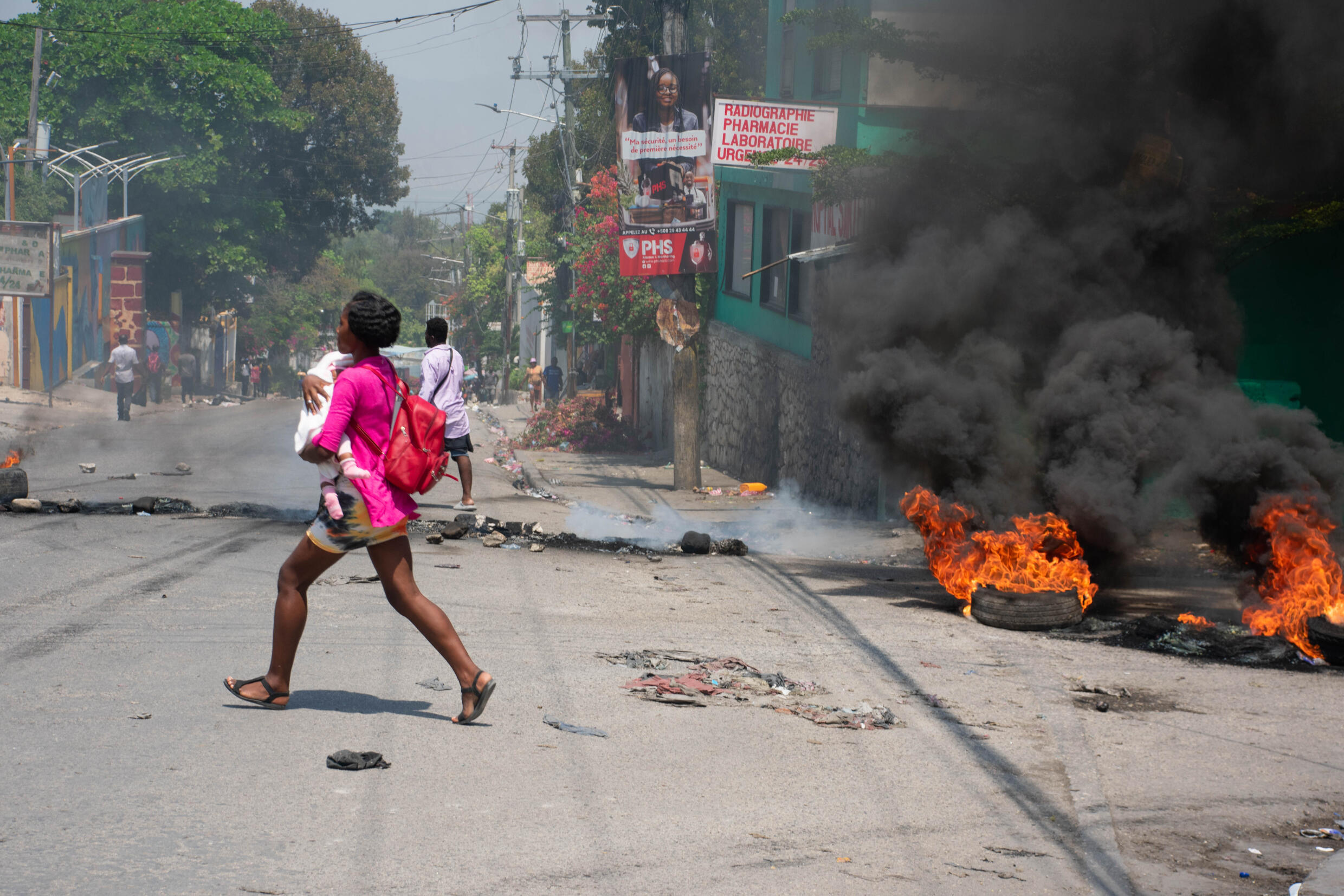 Une femme, un enfant dans les bras, court se mettre à l'abri pendant des tirs des bandes armées, le 20 mars 2024 à Port-au-Prince, en Haïti