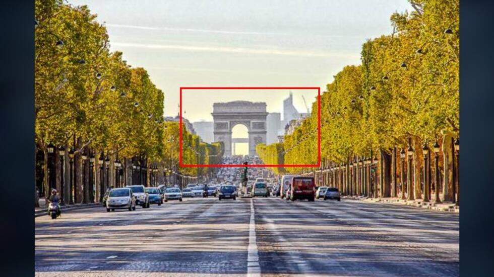 Photo de l’Arc de Triomphe prise depuis les Champs-Elysées. Encadrés en rouge : on aperçoit les immeubles de la Défense au loin.