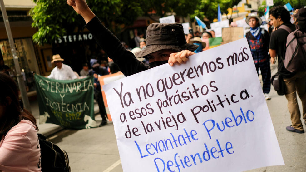 Una persona sostiene un cartel que dice "Ya no queremos esos parásitos de la vieja política. Párese pueblo defiéndase", mientras los manifestantes marchan hacia el Tribunal Supremo Electoral (TSE) exigiendo a las autoridades que respeten los resultados de la primera vuelta de Guatemala. El 8 de julio de 2023, en Ciudad de Guatemala, la capital.