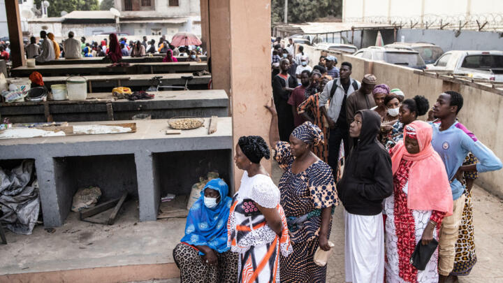 People wait in line before a voting station opened in a market in the Manjai Kunda neighbourhood in Banjul on December 4, 2021.