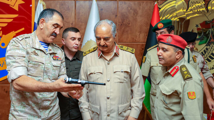 In this handout photo provided on August 24, 2023, Russia’s Deputy Defence Minister Yunus-bek Yevkurov is shown offering the gift of a pistol to Libyan military strongman Khalifa Haftar during an official visit to Benghazi. 