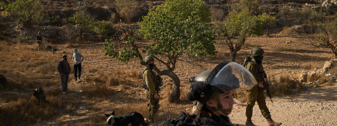 Israeli security forces block Palestinians from accessing an area for harvesting olives in the West Bank village of Sa'ir near Hebron on October 23, 2025, as Israeli settlers stand in the background.
