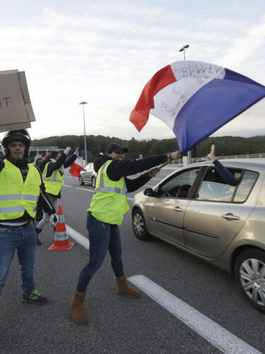 En esta fotografía de archivo del 19 de noviembre de 2018, manifestantes de los "chalecos amarillos" ondean una bandera francesa y un cartel con la leyenda «Peaje libre» mientras abren las barreras de peaje en una autopista en Antibes, en el sur de Francia.
