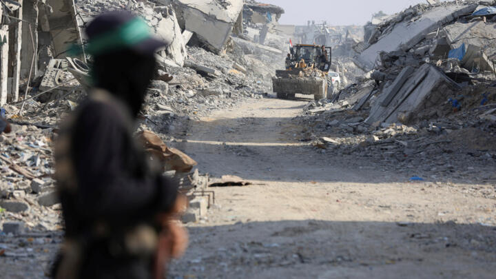 Machinery operates as a Palestinian Hamas militant stands guard near the so-called "yellow line" to which Israeli troops withdrew under the ceasefire agreement in Gaza City on November 2, 2025.