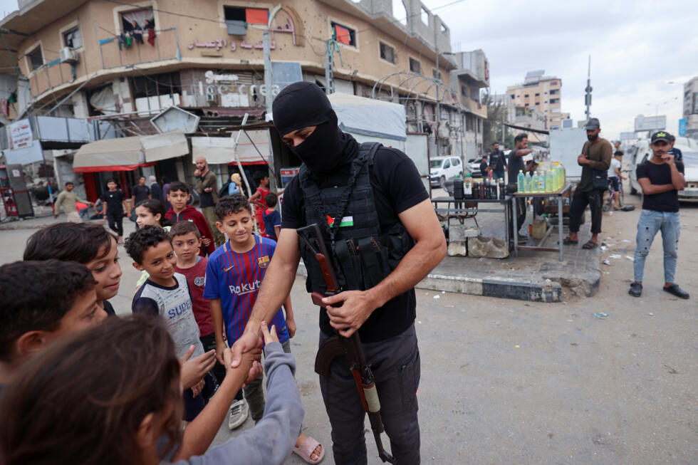 Un membre des forces de sécurité intérieure loyales au groupe palestinien Hamas salue de s enfants dans le camp de réfugiés de Nousseirat, dans le centre de la bande de Gaza, le 12 octobre 2025