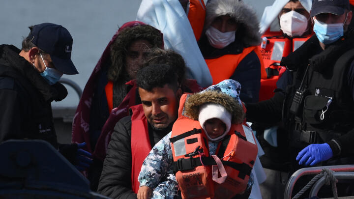 In this file photo taken on May 3, 2022, migrants, picked up at sea while attempting to cross the English Channel, are helped by a member of the UK Border Force to disembark from a boat, in the Marina at the Dover port, on the south-east coast of England. 