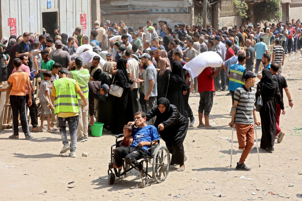 Une Palestinienne pousse un homme et un enfant en fauteuil roulant près d'un point de rassemblent pour recevoir des sacs de farine dans un entrepôt du Programme alimentaire mondial (PAM) à Gaza-ville, le 12 juillet 2025