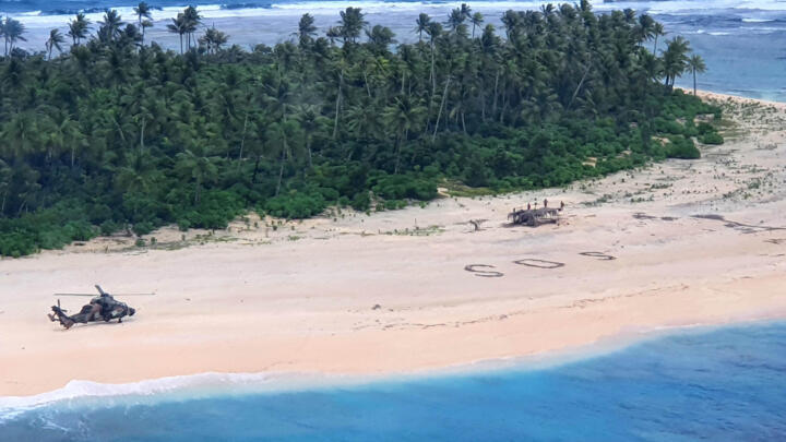 A handout photo from the Australian Defence Force shows a helicopter landing near the letters "SOS" on a beach on Pikelot Island, where the three men were rescued.