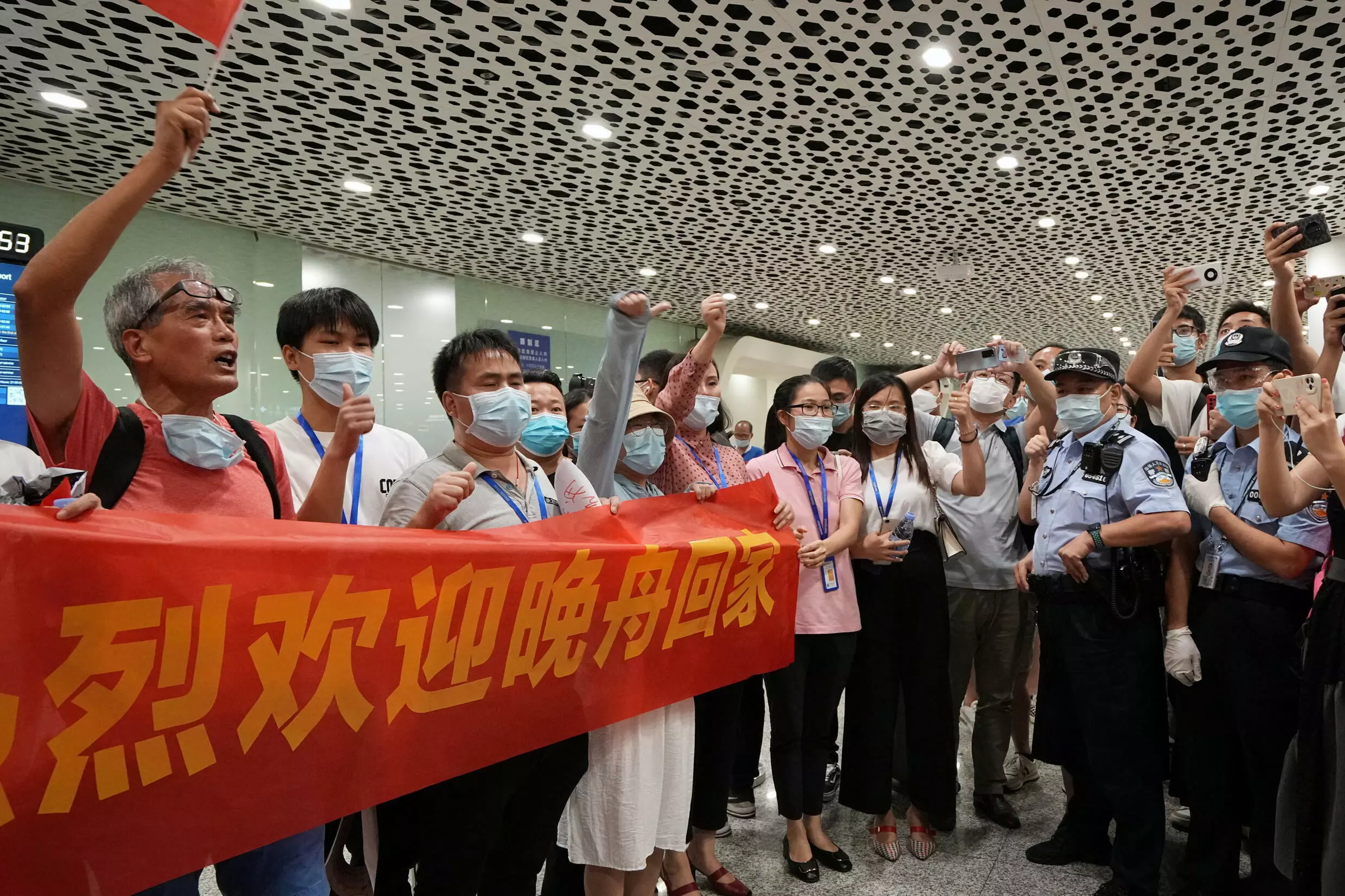 Agentes de policía se paran junto a los simpatizantes que sostienen una pancarta para dar la bienvenida a casa a la directora financiera de Huawei Technologies, Meng Wanzhou. Aeropuerto internacional Shenzhen Baoan en Shenzhen, provincia de Guangdong, China, el 25 de septiembre de 2021.