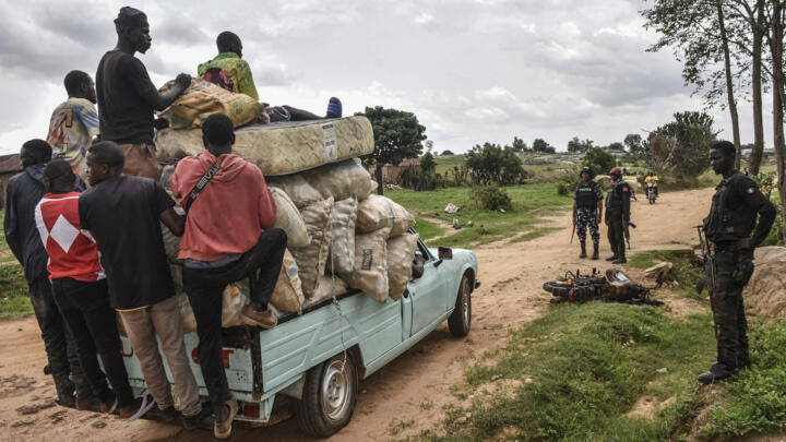 (FILE) Residents hang from the back of a pick-up truck while transporting their belongings as they reach a police chackpoint outside Mangu, near Jos in the Plateau State in Nigeria, on May 20, 2023 after fleeing unrest in central Nigeria.